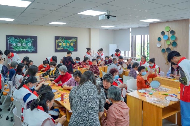 志愿者與殘障老人一起編織二十四節(jié)氣團扇。學校供圖